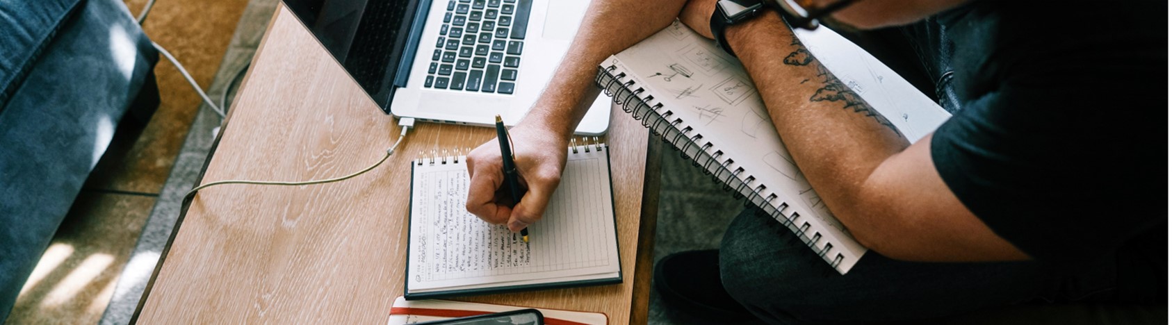 Man making notes on notepad with laptop nearby